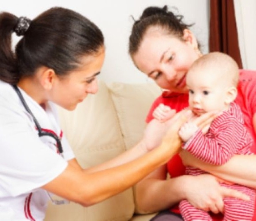 A mom holds up her young child while a health care professional examines the child.